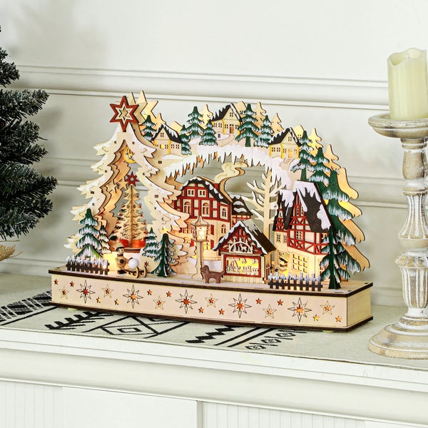 Beleuchtete Weihnachtsdekoration aus Holz mit winterlichem Dorf, Fachwerkhäusern und Tannen auf einem mit Sternen verzierten Sockel.