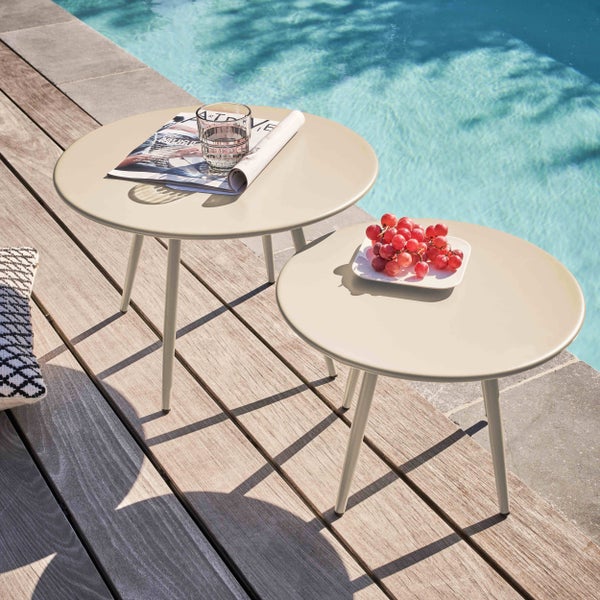 Zwei runde Beistelltische aus Metall auf einer Holzterrasse am Pool, einer mit Glas und Magazin, der andere mit Weintrauben.