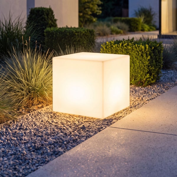 Beleuchteter Gartenwürfel als Außenleuchte in einem modernen Gartenbeet mit Kies und Pflanzen.