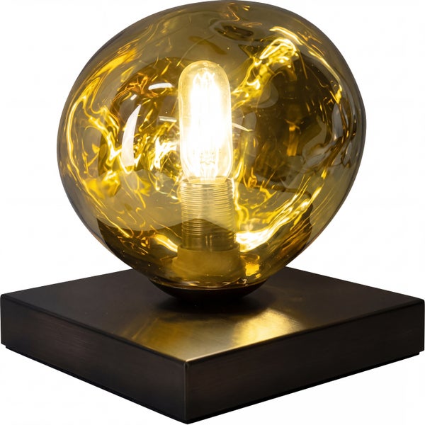 Tischleuchte mit quadratischem dunklem Metallsockel und unregelmäßiger bernsteinfarbener Glaskugel inklusive sichtbarem Leuchtmittel.