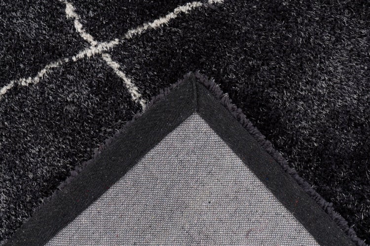 Nahaufnahme eines schwarzen Hochflor-Teppichs mit weißem geometrischem Muster und sichtbarer Rückseite.