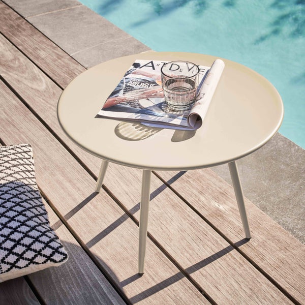 Runder Beistelltisch aus Metall auf einer Holzterrasse am Pool mit Magazin und Wasserglas in einer hellen, modernen Atmosphäre.