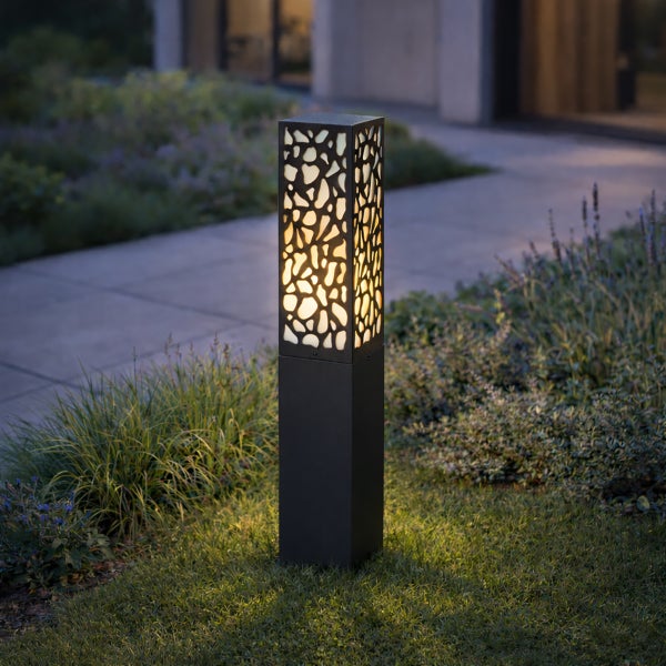 Moderne rechteckige Außen-Sockelleuchte mit organischem Ausschnittmuster und warmweißem Licht in einem Garten bei Dämmerung.