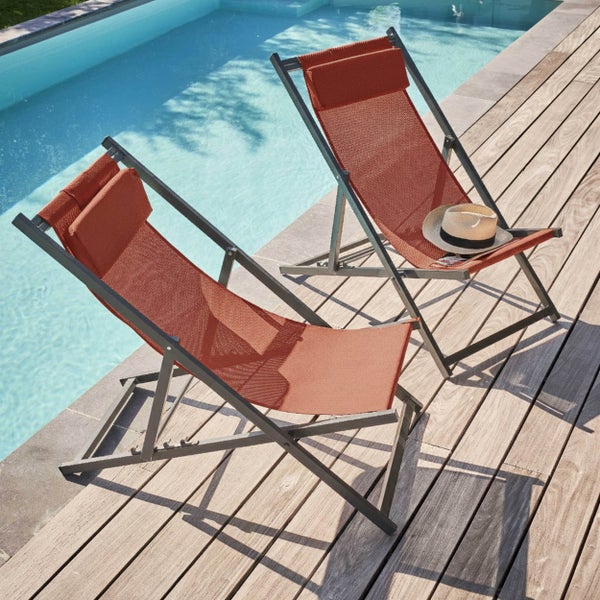 Zwei orangefarbene Liegestühle mit grauem Metallgestell auf einer Holzterrasse neben einem Swimmingpool.