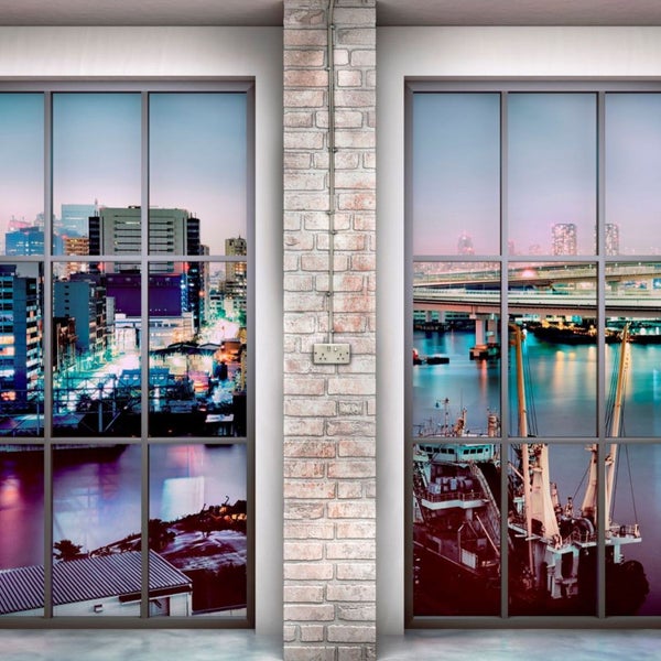 Zwei Fenster mit Blick auf eine Stadt bei Nacht, getrennt durch eine gemauerte Säule mit Steckdose.