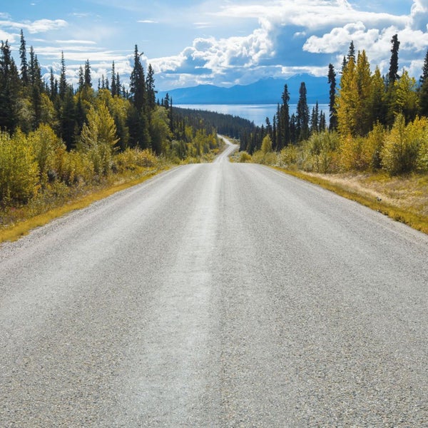 Eine lange Straße, umgeben von Bäumen und einem See in der Ferne.