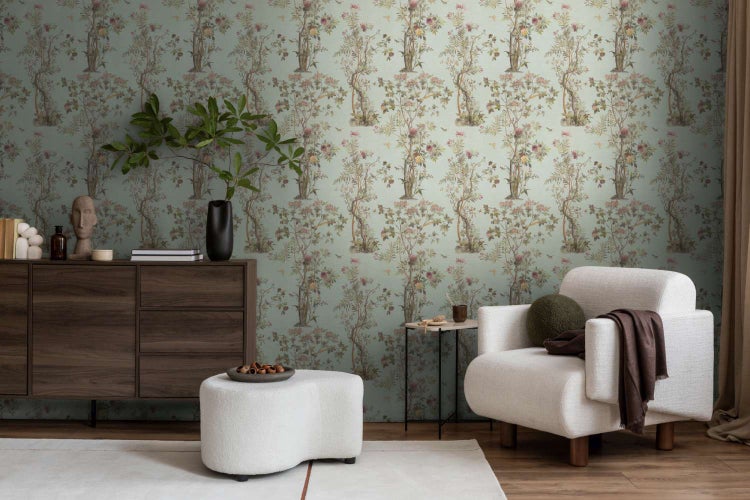 Wohnzimmer mit Vliestapete mit floralem Baummotiv in gedeckten Tönen, eingerichtet mit dunkler Kommode, hellem Sessel und organischem Hocker.