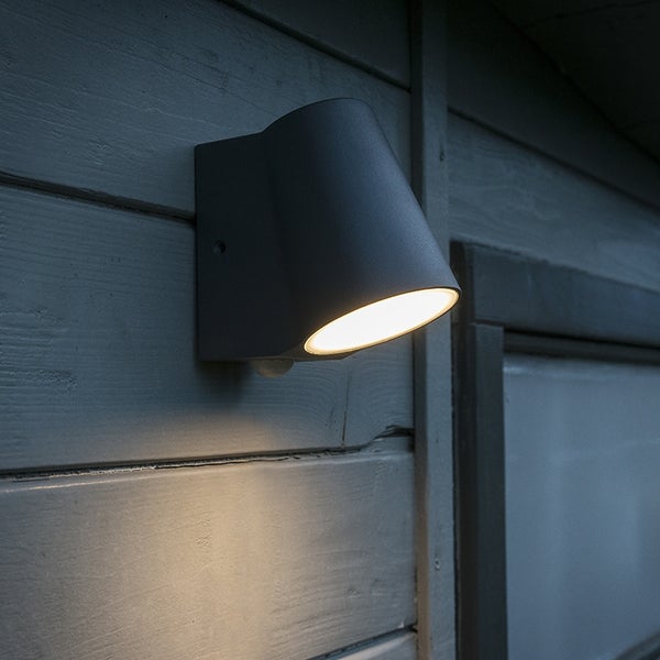 Moderne Außenwandleuchte mit Bewegungsmelder an einer Holzwand montiert, warmweißes LED-Licht strahlt nach unten.