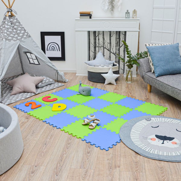 Helles Kinderzimmer mit Schaumstoff-Spielmatte, grauem Tipi-Zelt, Sofa, Bällebad und rundem Teppich mit Löwenmotiv auf hellem Holzboden.