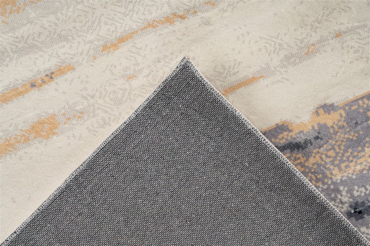 Teppich mit abstraktem Muster in Beige, Gold und Grau sowie einer umgeknickten Ecke, die die dunkle, strukturierte Rückseite zeigt.