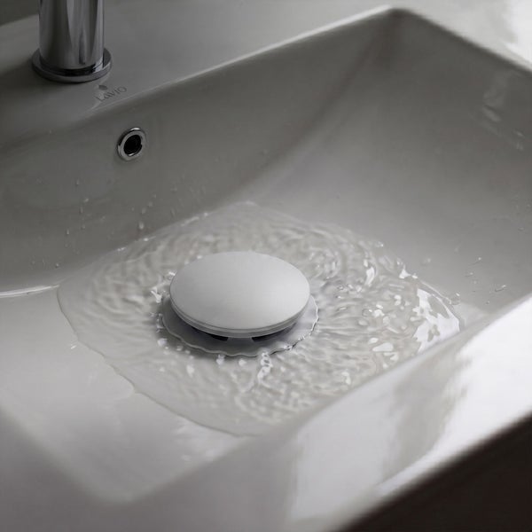 Ein runder, weißer Universal-Abflussstopfen in einem Waschbecken aus Keramik, umgeben von fließendem Wasser.