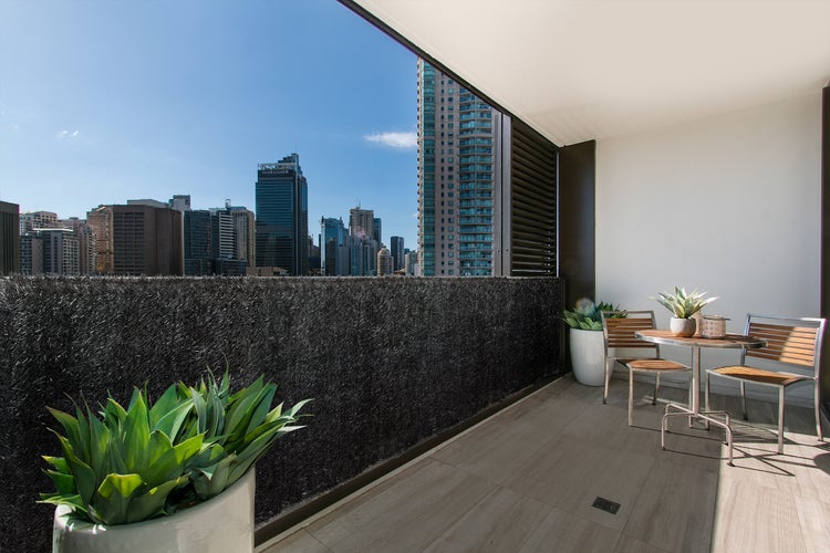 Moderner Balkon mit dunklem Sichtschutz am Geländer, Sitzgruppe aus Holz und Metall sowie Topfpflanzen vor einer Skyline.