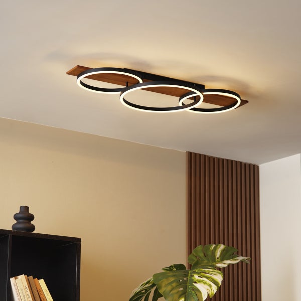 Moderne LED Deckenleuchte mit drei ringförmigen Leuchtelementen auf einem Holzbalken für eine wohnliche Raumbeleuchtung.