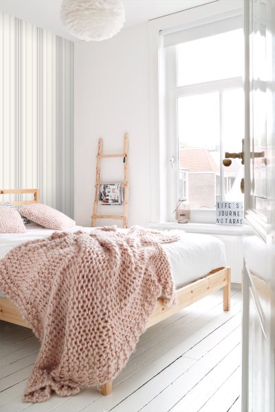 Helles Schlafzimmer mit Bett, Strickdecke und dekorativer Leiter