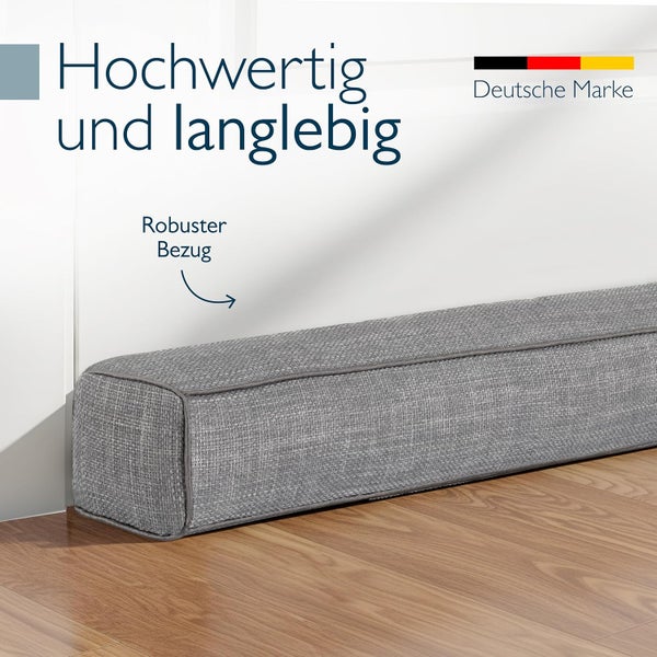 Grauer Zugluftstopper aus robustem Stoff auf Holzfußboden, hochwertige und langlebige Qualität, deutsche Marke.