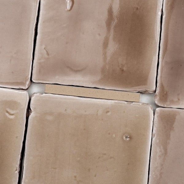 Quadratische Wandfliesen mit glänzender, strukturierter Oberfläche in beige-brauner Optik, verlegt mit deutlicher Fuge.