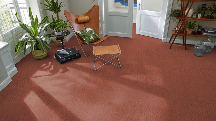 Helles Wohnzimmer mit Teppichfliesen in Rippenstruktur, einem Schmetterlingsstuhl aus Leder und Zimmerpflanzen.