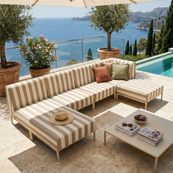 Modernes Garten-Lounge-Set mit gestreiftem Sofa und Hockern auf einer Terrasse am Pool mit Meerblick, Steinboden und Olivenbäumen.