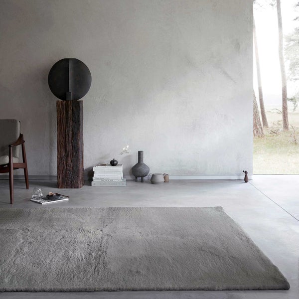 Großer, weicher Hochflor-Teppich in einem hellen, minimalistischen Raum mit strukturierten Wänden, Betonboden und moderner Dekoration.