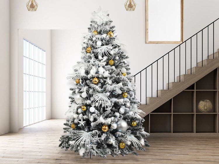 Ein geschmückter, künstlicher Weihnachtsbaum mit Schnee-Effekt steht in einem modernen, hellen Wohnraum neben einer Treppe.