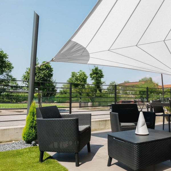 Weißes Sonnensegel über einer Terrasse mit dunklen Rattan-Sesseln und einem Tisch.