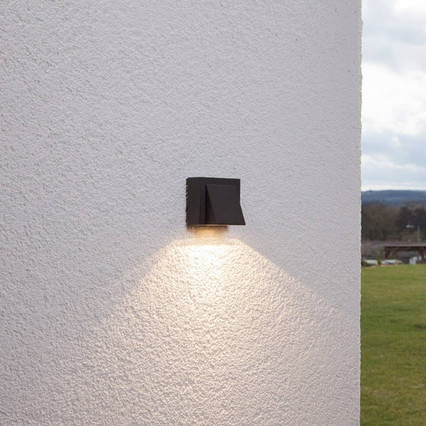 Moderne Außenwandleuchte in Anthrazit an einer weißen Hauswand mit nach unten gerichtetem Lichtkegel.