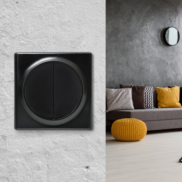 Ein moderner Lichtschalter in quadratischer Form mit rundem Einsatz, montiert an einer Wand, daneben ein Ausschnitt eines modernen Wohnzimmers.