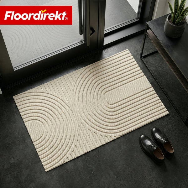 Floordirekt Logo. Rechteckige Fußmatte mit geometrischem dreidimensionalem Muster vor einer Glastür mit Schuhen und einer Pflanze.