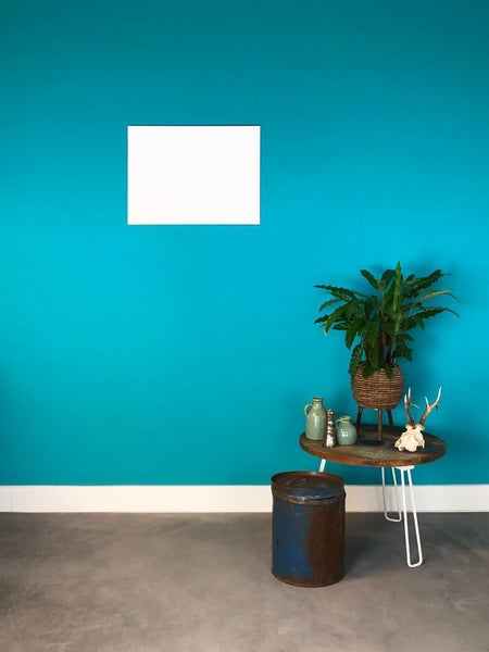 Modern gestalteter Raum mit türkis gestrichener Wand, weißem Bilderrahmen, Holzbeistelltisch mit Zimmerpflanze und Metalldekoration.