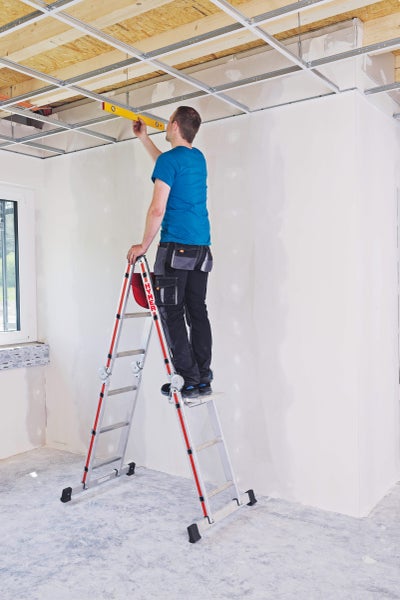 Mann auf einer Mehrzweckleiter, der eine Deckenkonstruktion mit einer Wasserwaage ausrichtet