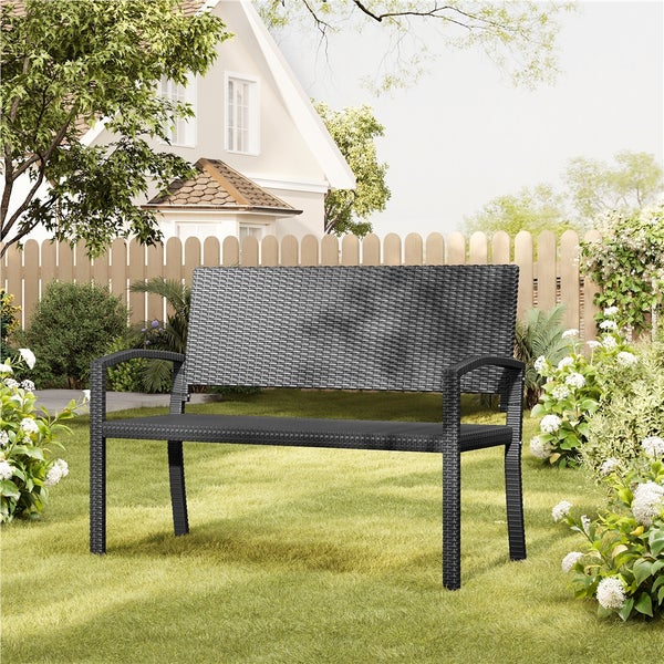 Gartenbank aus Polyrattan-Geflecht in einem gepflegten Garten auf einer Rasenfläche vor einem Holzzaun.