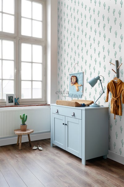 Ein Kinderzimmer mit einer Kommode, einer Lampe, einem Hocker und einer Kaktus-Tapete.