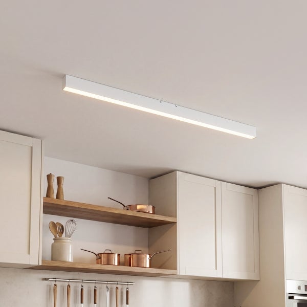 Moderne schmale LED Deckenleuchte in einer hellen Küche mit Küchenschränken und offenen Regalen mit Kupfergeschirr.