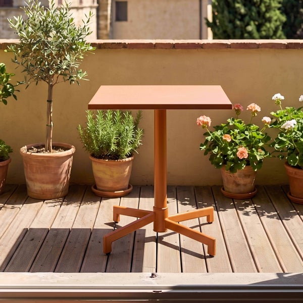 Quadratischer Bistrotisch aus Metall auf einer sonnigen Terrasse mit Holzdeck und verschiedenen Topfpflanzen.