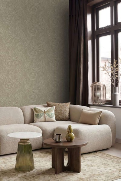 Wohnzimmer mit beigefarbener Tapete mit Palmenblattmuster, beigem Sofa und zwei Couchtischen vor einem Fenster mit dunklen Vorhängen.
