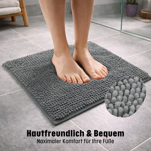 Füße auf einer weichen grauen Badematte aus Chenille in einem hellen Badezimmer mit Fliesenboden.