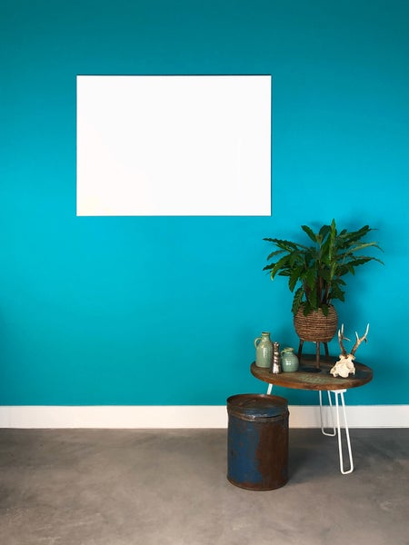 Wohnbereich mit türkisfarbener Wand, weißem Wandelement, Holztisch mit Zimmerpflanze, Metalldose und grauem Betonboden.