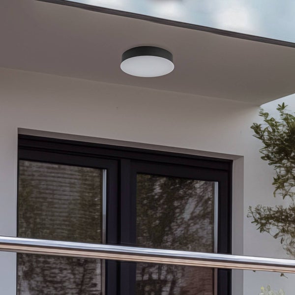Runde LED-Außen-Deckenleuchte mit schwarzem Gehäuse und weißem Diffusor, montiert an einem Dachvorsprung über einem dunklen Fensterrahmen.
