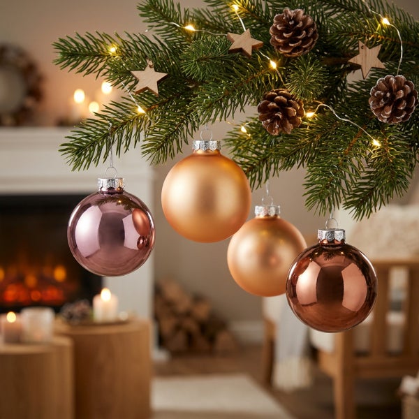 Weihnachtskugeln in verschiedenen Oberflächen hängen an einem geschmückten Tannenbaum vor einem Kamin im Wohnzimmer.