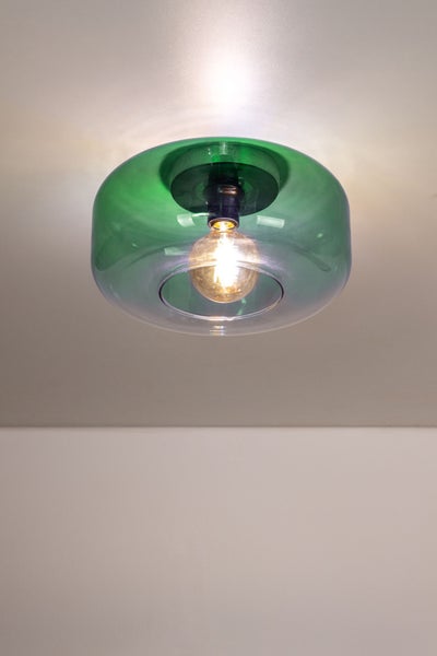 Runde Deckenleuchte aus grünem Glas mit brennender Glühbirne an einer weißen Decke.