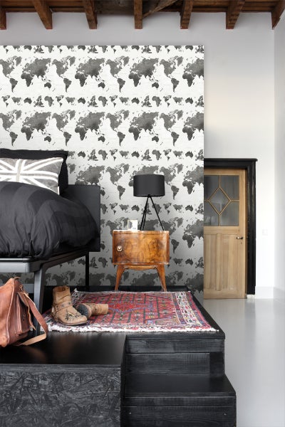 Schlafzimmer mit Bett, Nachttisch und Tapete mit Weltkartenmuster