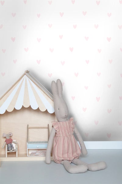 Kinderzimmer-Szene mit Spielhaus, Hasenpuppe und Mauspuppe vor einer Wand mit Herzmuster