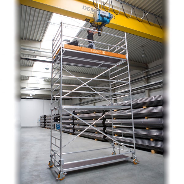 Aufnahme eines Bauarbeiters auf einem Layher Fahrgerüst in einer Werkshalle.