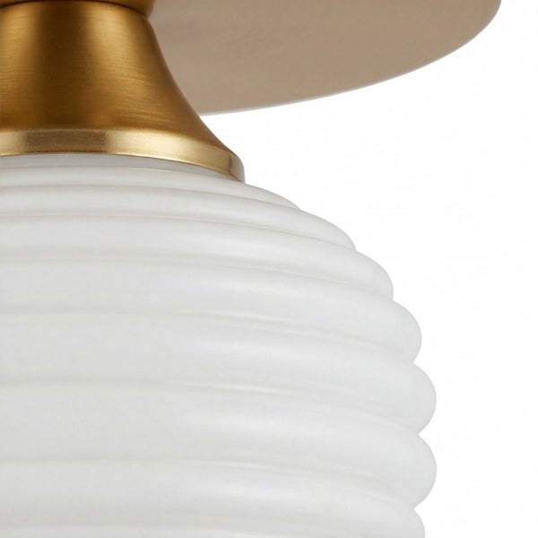 Detailansicht einer Lampe mit weißem geriffeltem Glasschirm und Metallhalterung in Messingoptik.