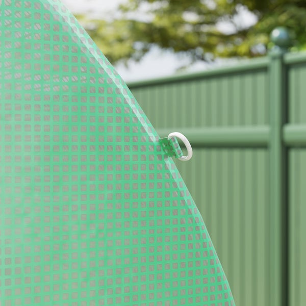 Nahaufnahme einer grünen Gitterfolie für Gewächshäuser mit weißem Befestigungsring vor einem Gartenzaun.