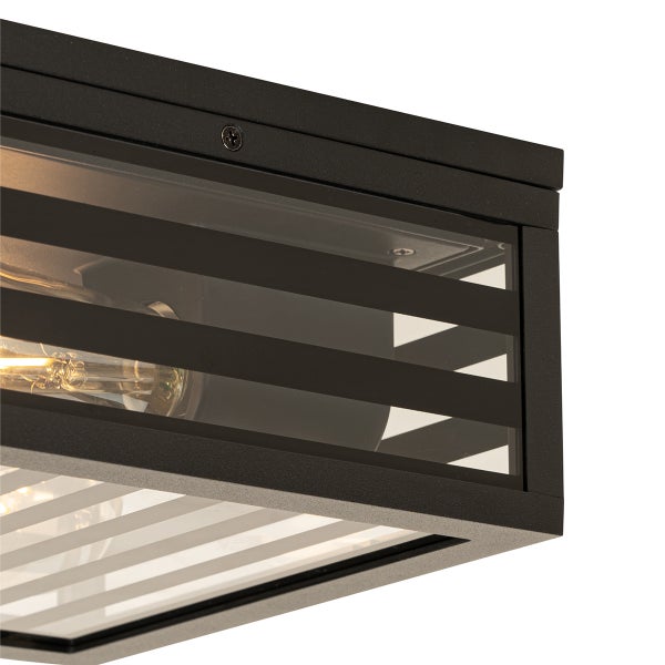 Nahaufnahme einer rechteckigen Leuchte mit schwarzem Metallrahmen und gestreiftem Glaseinsatz sowie sichtbarem Leuchtmittel.