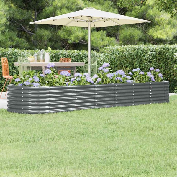 Hochbeet aus Wellblech in Anthrazit, bepflanzt mit blauen Hortensien, im Hintergrund ein Gartentisch mit Stühlen und Sonnenschirm.