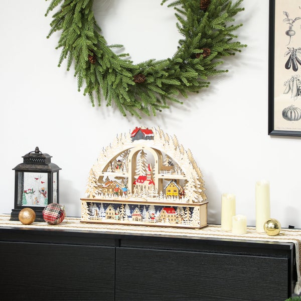 Weihnachtliche Szene mit einem hölzernen Schwibbogen, einem Tannenkranz, einer Laterne und Kerzen auf einem Sideboard.