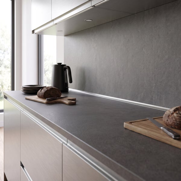Moderne Küchenzeile mit dunkler Arbeitsplatte, strukturierter Rückwand, Holzschneidebrettern und Wasserkocher in einem hellen Raum.