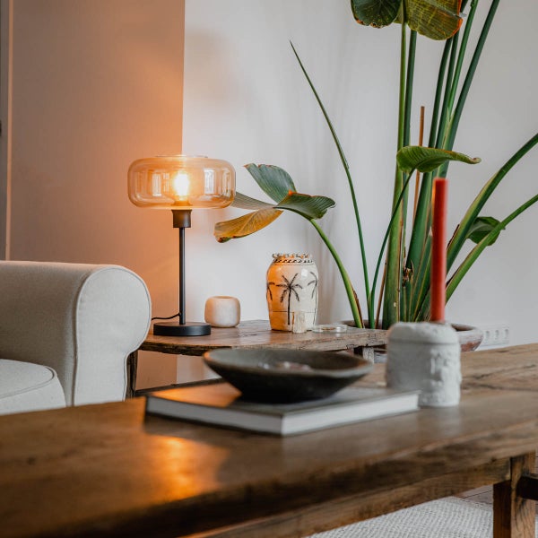 Wohnzimmer mit Tischleuchte, Pflanze und dekorativen Elementen auf einem Holztisch